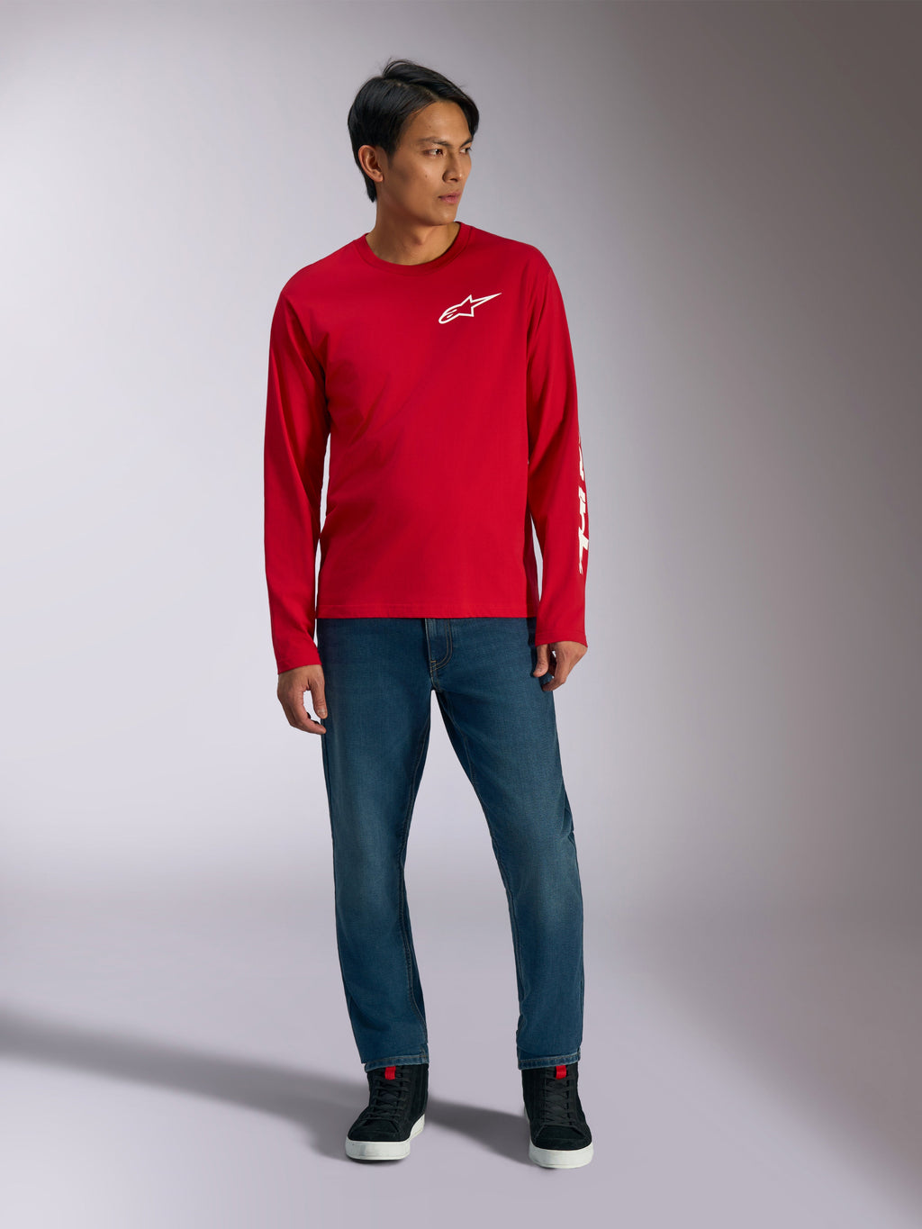 Alpinestars Trackside CSF Tee, camiseta de manga larga, roja con logotipo Alpinestars blanco, foto de estilo de vida combinada con vaqueros azules y zapatillas negras, ropa deportiva casual inspirada en el automovilismo