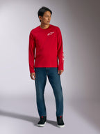 Alpinestars Trackside CSF Tee, camiseta de manga larga, roja con logotipo Alpinestars blanco, foto de estilo de vida combinada con vaqueros azules y zapatillas negras, ropa deportiva casual inspirada en el automovilismo