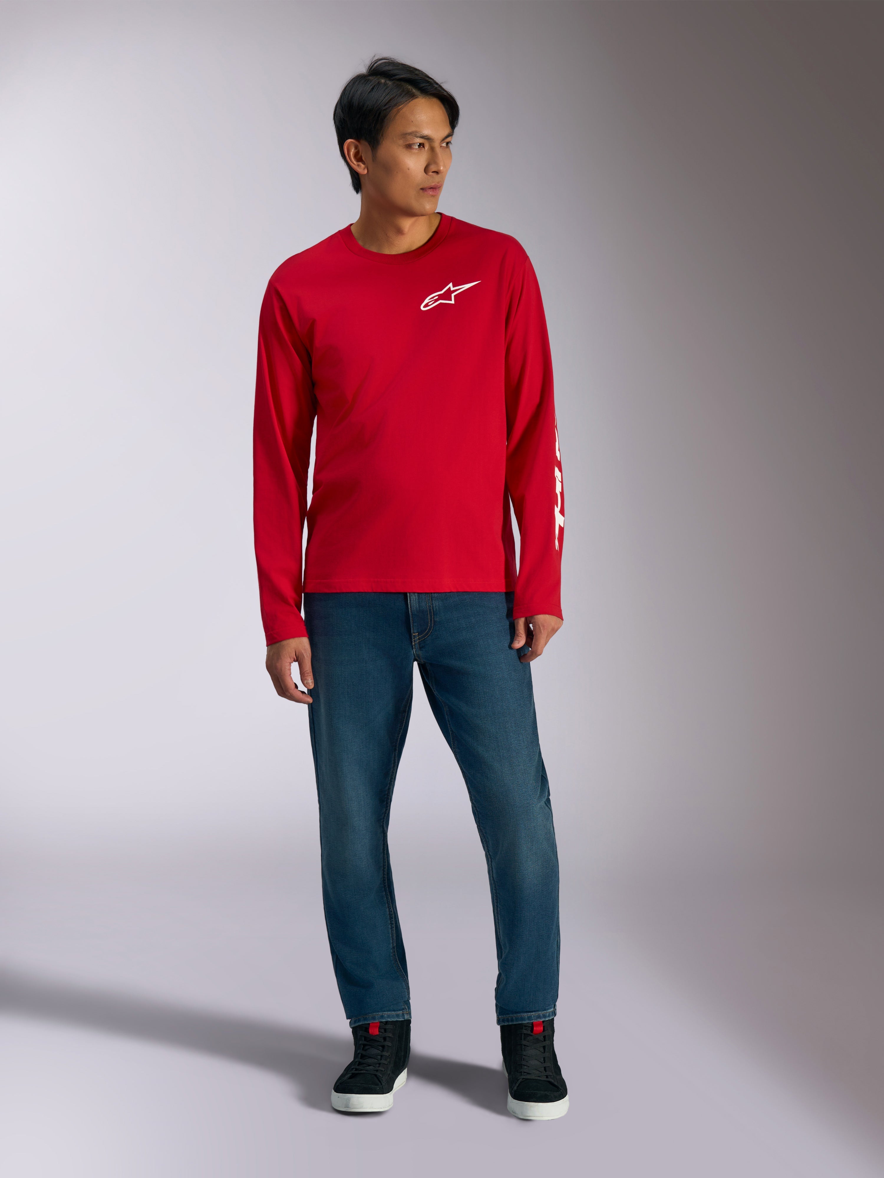 Alpinestars Trackside CSF Tee, camiseta de manga larga, roja con logotipo Alpinestars blanco, foto de estilo de vida combinada con vaqueros azules y zapatillas negras, ropa deportiva casual inspirada en el automovilismo