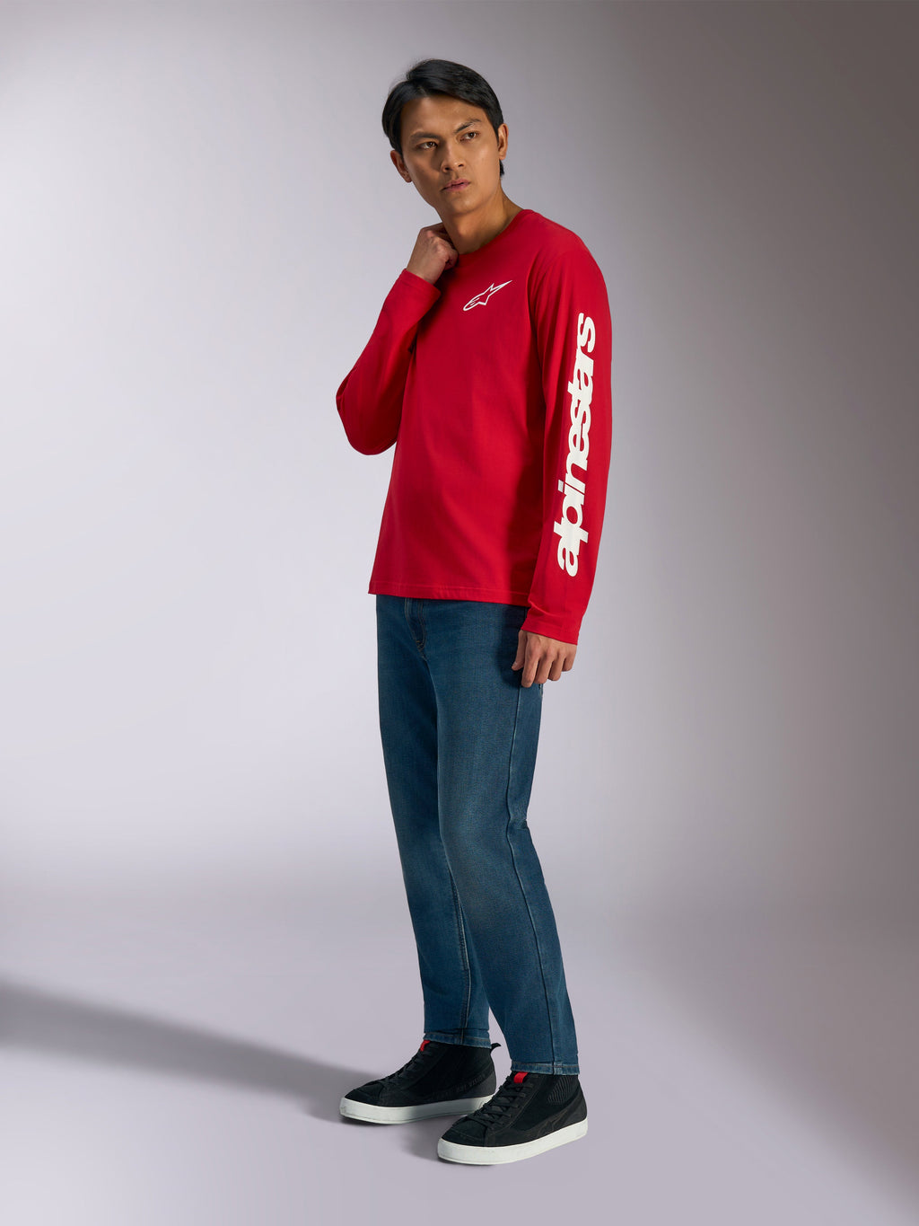 Camiseta de manga larga Alpinestars Trackside CSF, roja con logotipos Alpinestars blancos en el pecho y la manga, usada por un modelo con jeans azules y zapatillas negras, ropa urbana informal inspirada en el automovilismo