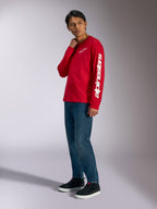 Camiseta de manga larga Alpinestars Trackside CSF, roja con logotipos Alpinestars blancos en el pecho y la manga, usada por un modelo con jeans azules y zapatillas negras, ropa urbana informal inspirada en el automovilismo