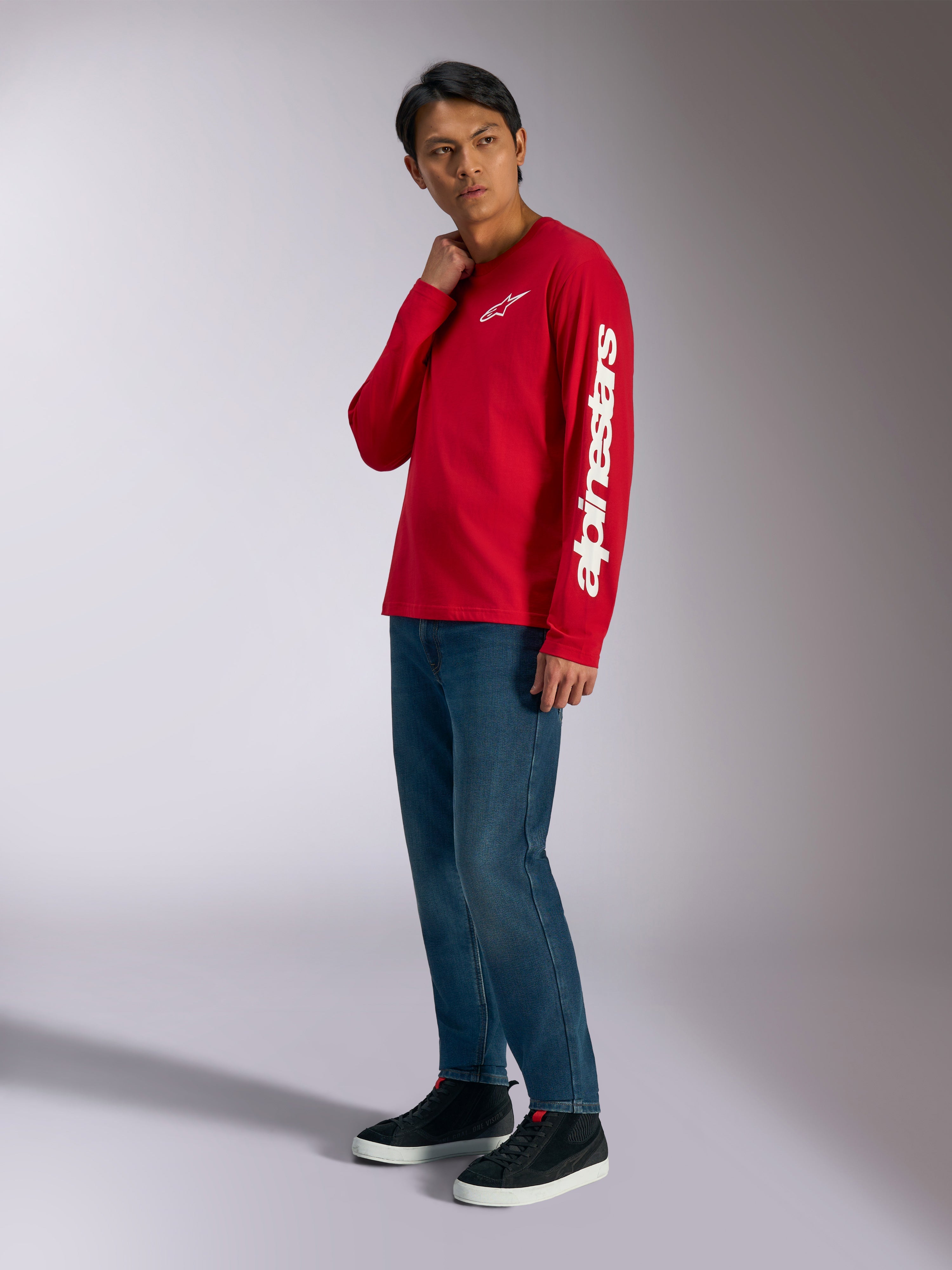 Camiseta de manga larga Alpinestars Trackside CSF, roja con logotipos Alpinestars blancos en el pecho y la manga, usada por un modelo con jeans azules y zapatillas negras, ropa urbana informal inspirada en el automovilismo