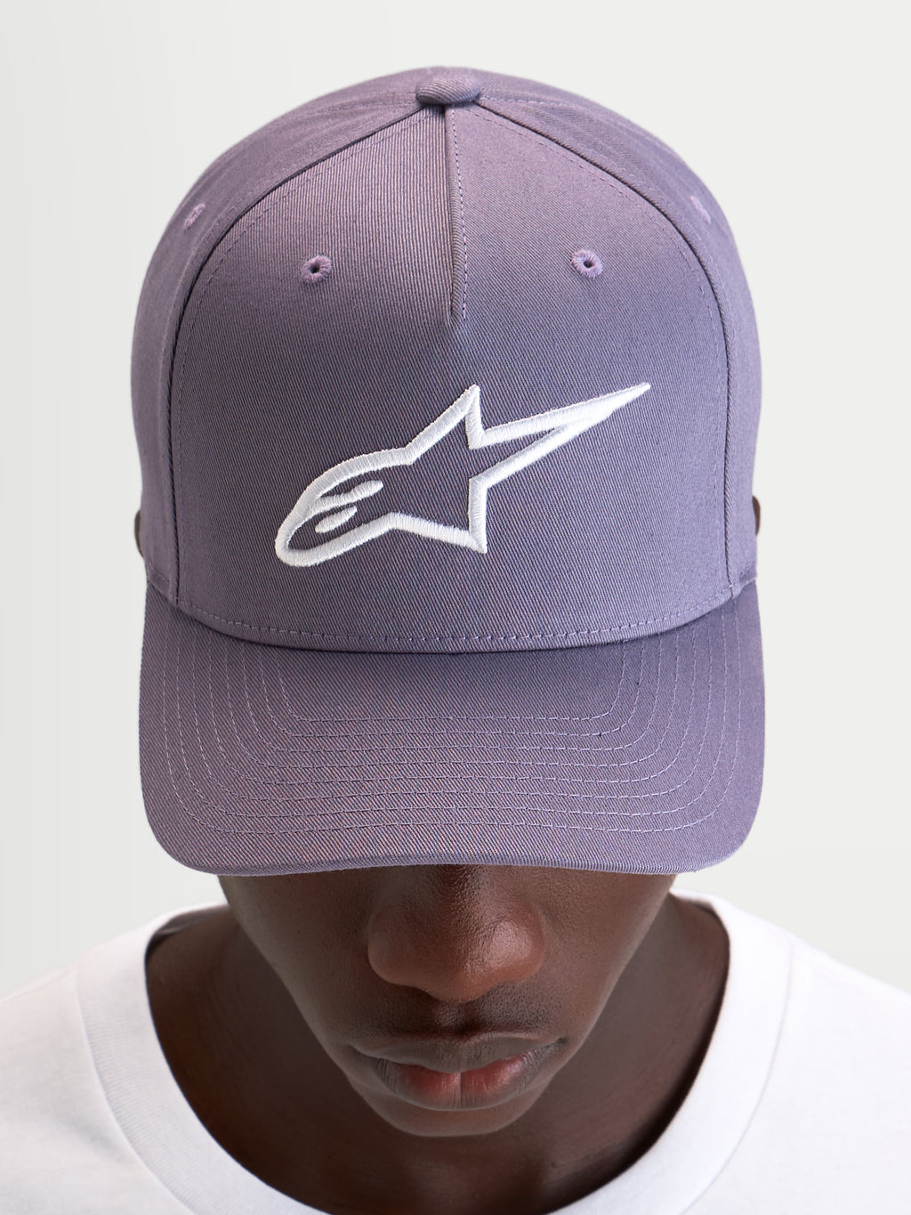 Gorra Ageless Snapback Alpinestars, gorra sportswear casual, morada y blanca, con visera curva, corona estructurada y logotipo Astars bordado en 3D en la parte delantera, vista frontal en modelo
