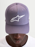 Gorra Ageless Snapback Alpinestars, gorra sportswear casual, morada y blanca, con visera curva, corona estructurada y logotipo Astars bordado en 3D en la parte delantera, vista frontal en modelo
