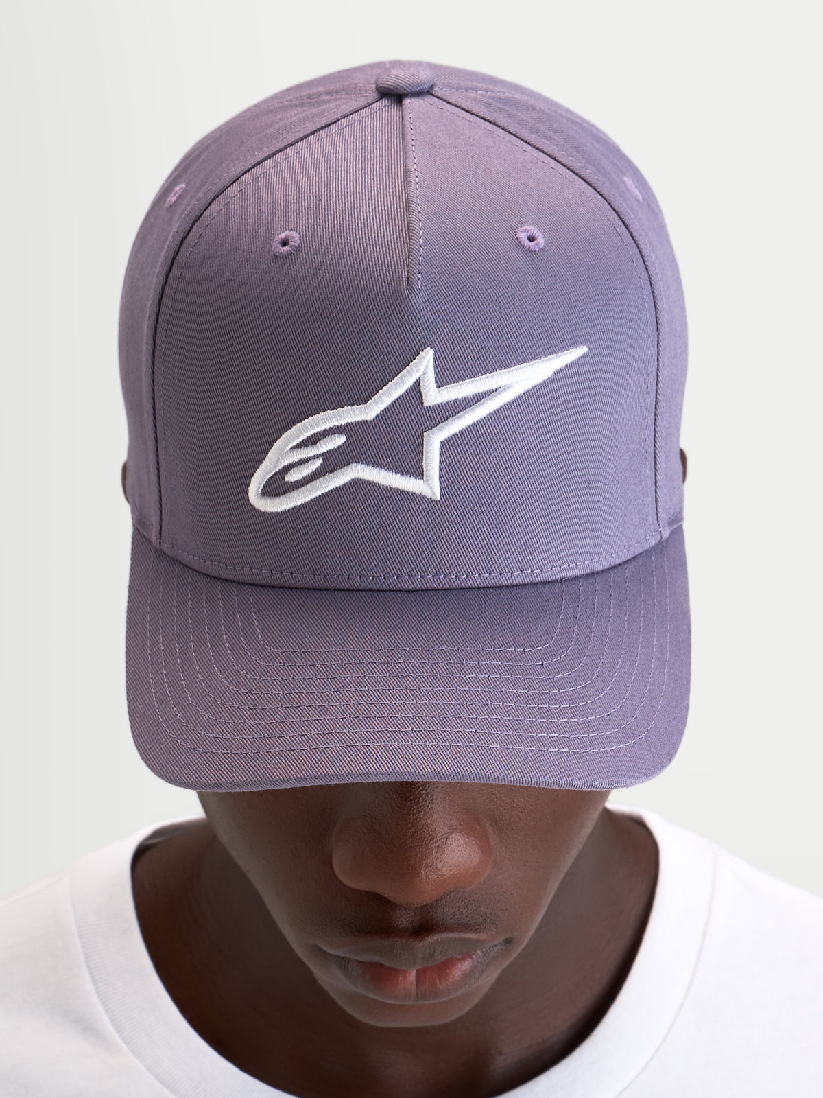 Gorra Ageless Snapback Alpinestars, gorra sportswear casual, morada y blanca, con visera curva, corona estructurada y logotipo Astars bordado en 3D en la parte delantera, vista frontal en modelo