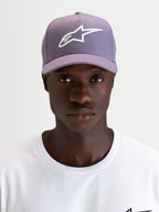 Gorra Ageless Snapback Alpinestars, gorra deportiva con visera curva, morada y blanca, con el logo Astars bordado en 3D en el panel frontal, vista frontal en modelo