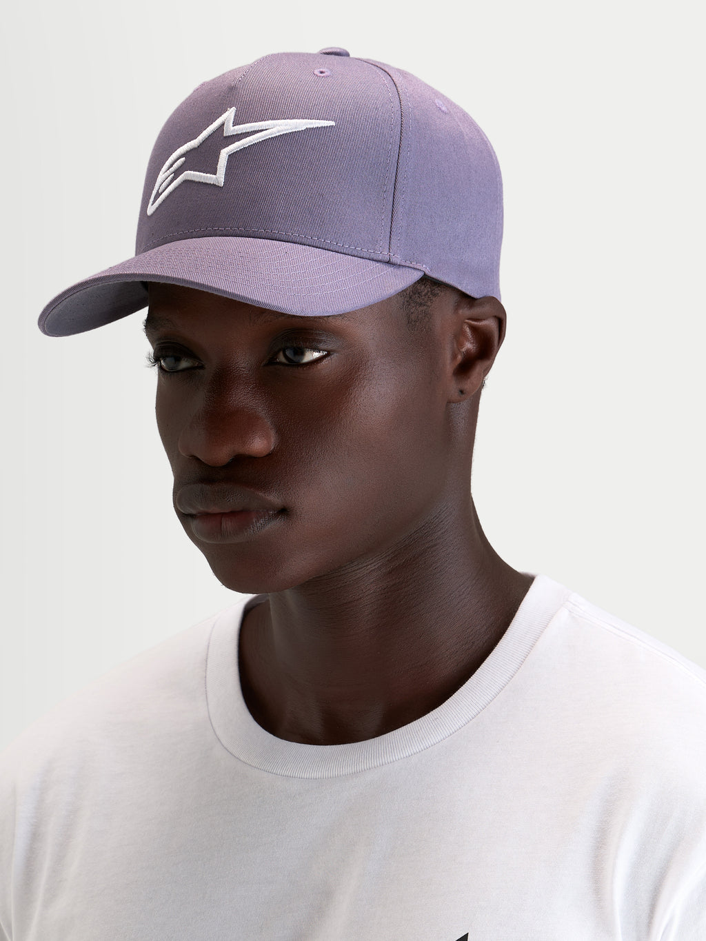 Gorra Ageless Snapback Alpinestars, gorra deportiva en morado polvoriento y blanco, con visera curva y corona estructurada, vista en modelo
