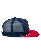 Gorra Alpinestars Control Trucker, azul marino y roja, vista de perfil lateral que muestra la parte delantera de sarga azul marino y paneles traseros de malla, visera plana roja con detalle de cuerda trenzada blanca, accesorio casual inspirado en el automovilismo
