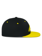 Gorra Snapback Alpinestars Thickness, vista de perfil lateral, corona negra con visera plana y ojales en amarillo de alta visibilidad, logotipo bordado en 3D en la parte frontal, accesorio de cabeza casual inspirado en el automovilismo
