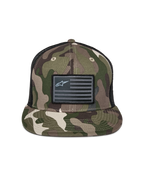 Gorra Alpinestars Flag Flat Trucker, camuflaje verde y negro, visera plana con corona estructurada, parche de bandera negra con el logo de Alpinestars, parte trasera de malla, accesorio casual inspirado en el automovilismo