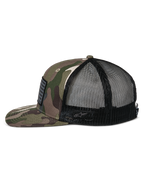 Gorra Alpinestars Flag Flat Trucker, camuflaje verde y negro, visera plana y corona estructurada, frente de sarga de camuflaje con malla trasera negra, vista lateral que muestra el parche de bandera merrow y el logotipo bordado, estilo urbano casual inspirado en el automovilismo