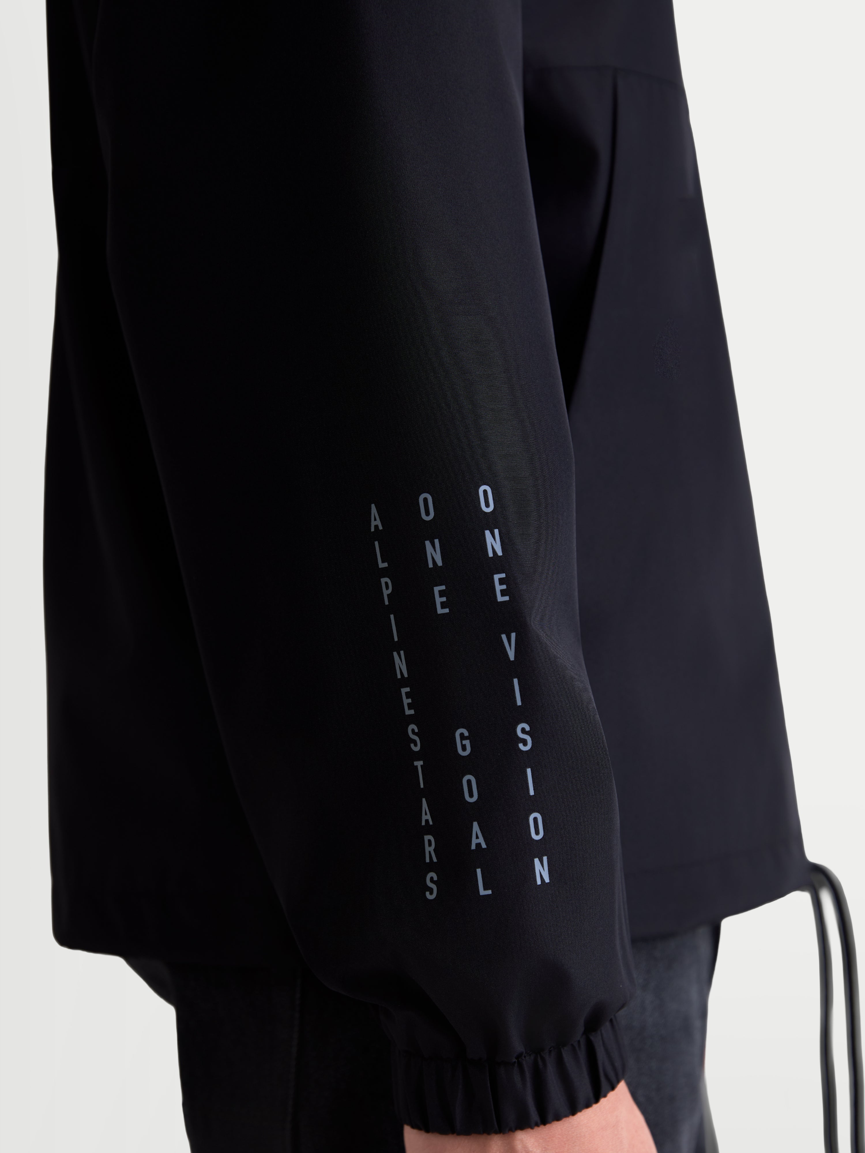 Alpinestars Speeder Resolve, chaqueta cortavientos negra, primer plano de la manga con logotipo vertical y puño elástico, construcción ligera de poliéster para uso urbano