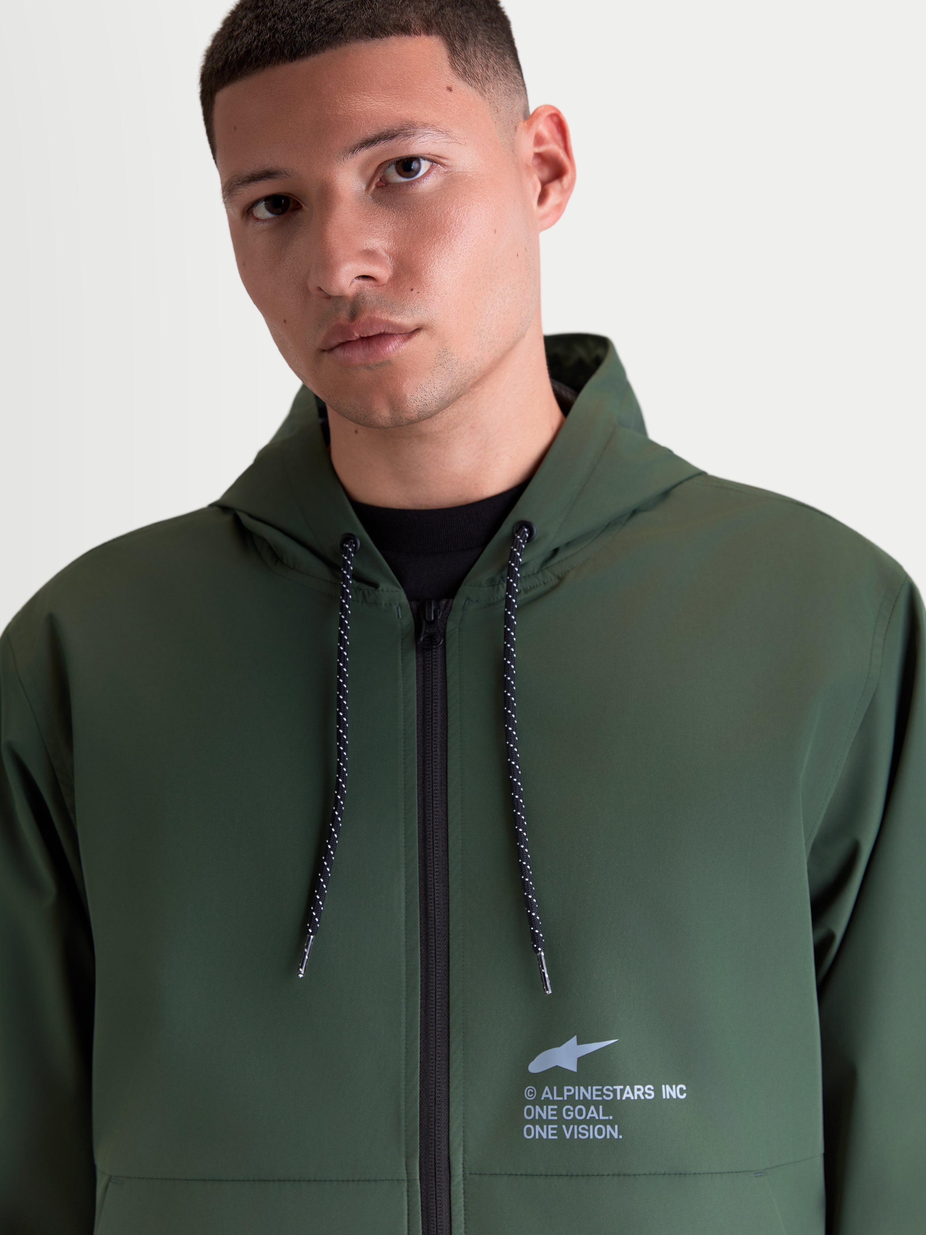 Alpinestars Speeder Resolve, chaqueta cortavientos para hombre en color verde, con capucha ajustable, cordones moteados y logotipo Alpinestars en el pecho, prenda ligera de estilo deportivo y casual.