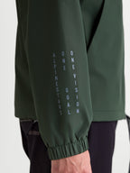 Alpinestars chaqueta cortavientos Speeder Resolve, cortavientos ligero de ropa deportiva en verde pino, primer plano de la manga con marca vertical de Alpinestars, lema One Goal One Vision y detalle de puño elástico.