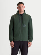 Alpinestars Chaqueta cortavientos Speeder Resolve, ropa deportiva ligera para uso urbano, chaqueta con capucha para hombre en verde pino con interior con forro de malla, capucha ajustable con cordón y cremallera frontal completa, marca Alpinestars en el pecho, vista frontal en modelo.