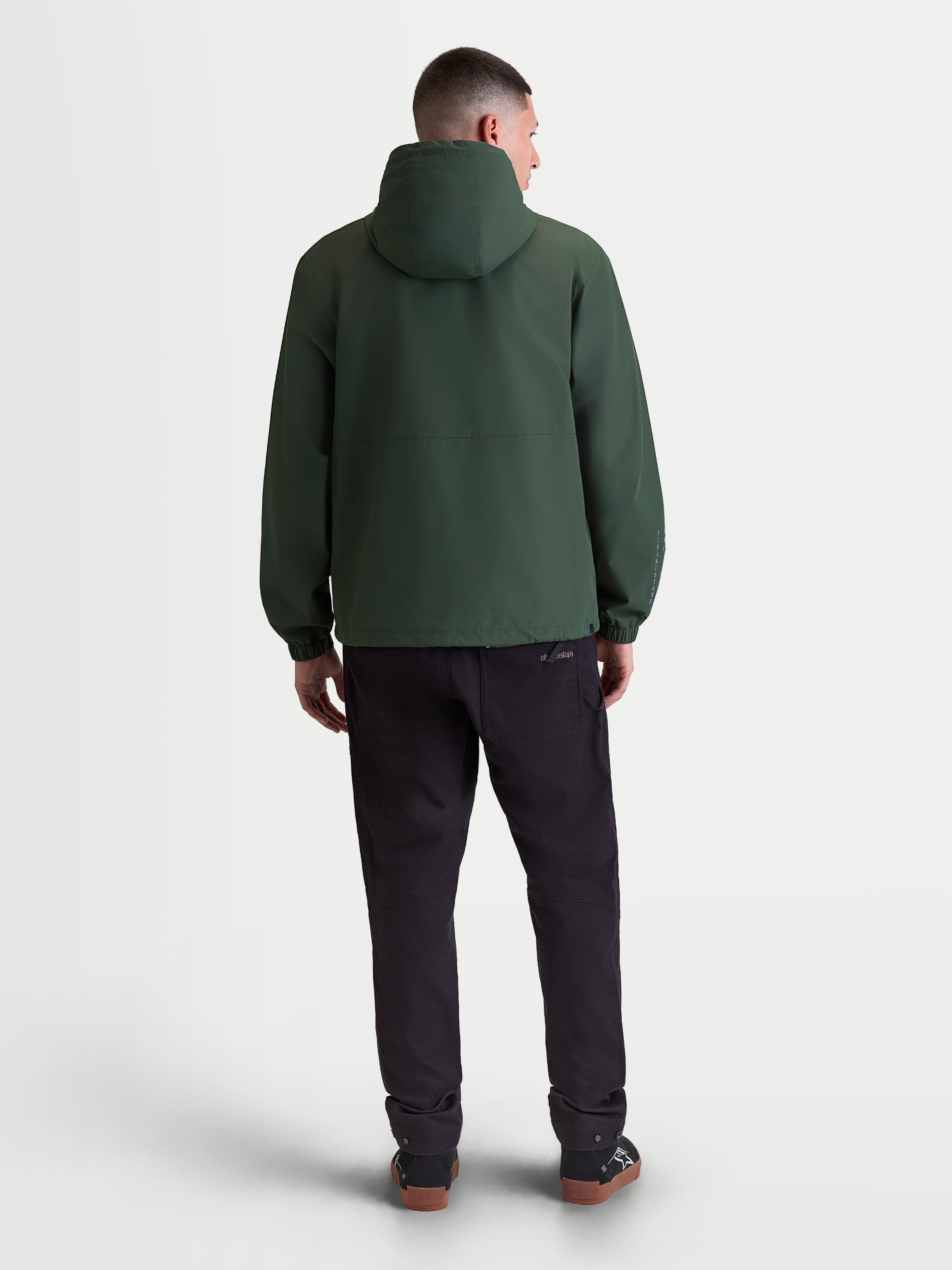 Alpinestars chaqueta cortavientos Speeder Resolve, chaqueta ligera de sportswear para hombre en color verde pino, diseño de textil cortavientos, vista trasera que muestra la capucha y los puños elásticos.