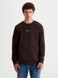 Alpinestars Guise Oversize, sudadera de forro polar con cuello redondo, ajuste relajado unisex mostrado en modelo, color marrón, confeccionada en algodón y poliéster reciclado, con bolsillo canguro y logotipos bordados en el pecho y la manga, estilo casual inspirado en el motorsport.