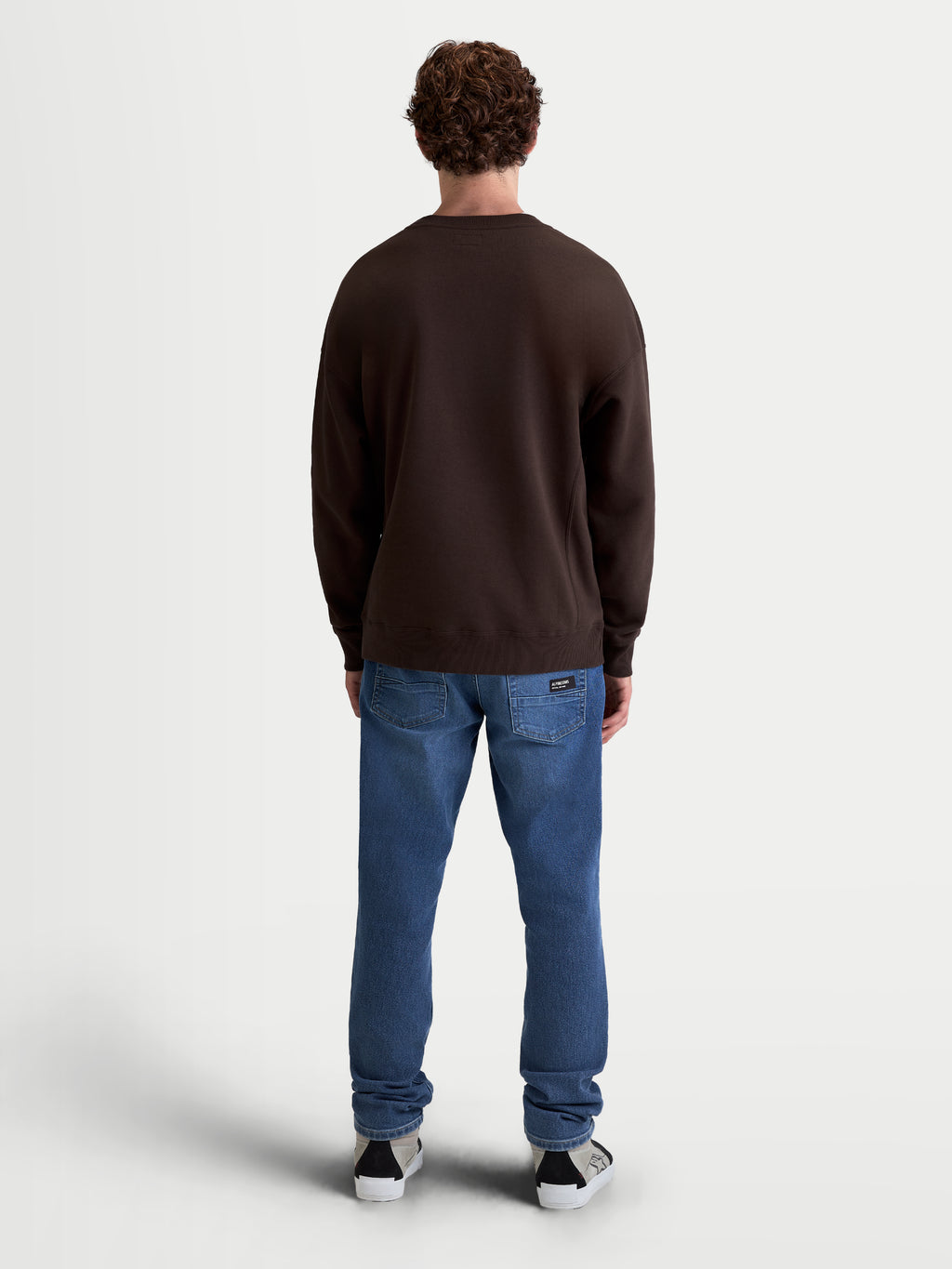 Alpinestars Sudadera Guise Oversize, vista trasera en modelo, sudadera marrón de cuello redondo con ajuste relajado, confeccionada en mezcla de algodón y poliéster reciclado, puños y dobladillo de canalé, estilo casual inspirado en el motorsport.