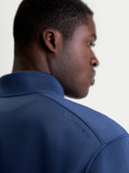 Alpinestars Sudadera Apera Half-Zip, sudadera de sportswear en azul acero, vista de primer plano de la espalda sobre modelo que muestra el logotipo Alpinestars HD tonal en el hombro y el tejido de forro polar premium de mezcla triple