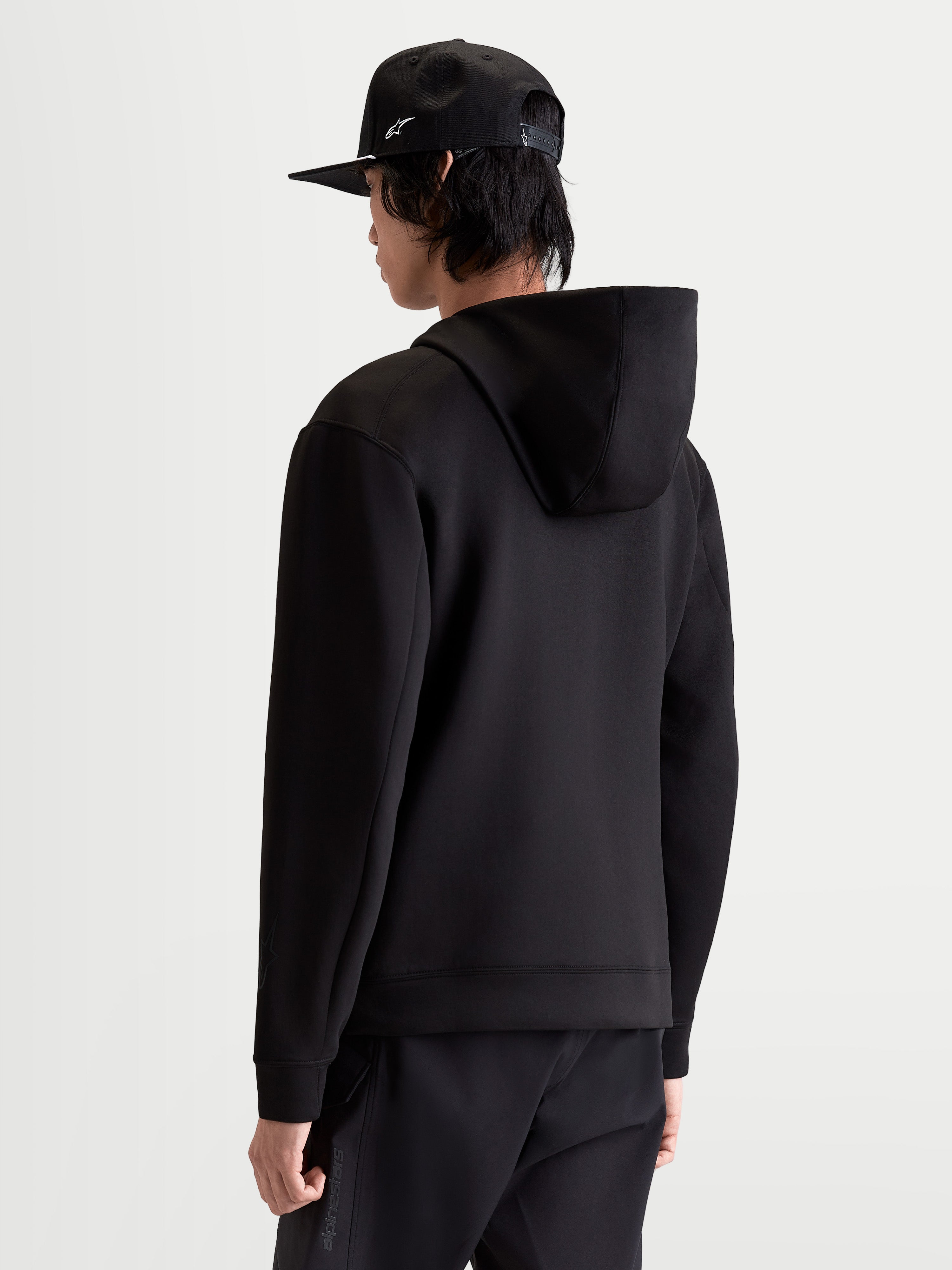 Alpinestars Sudadera con Capucha Datrix, sudadera tipo pulóver de ropa deportiva para hombre, color negro, vista trasera en modelo que muestra la construcción de forro polar de doble cara y capucha con forro de malla, estilo casual inspirado en el motorsport