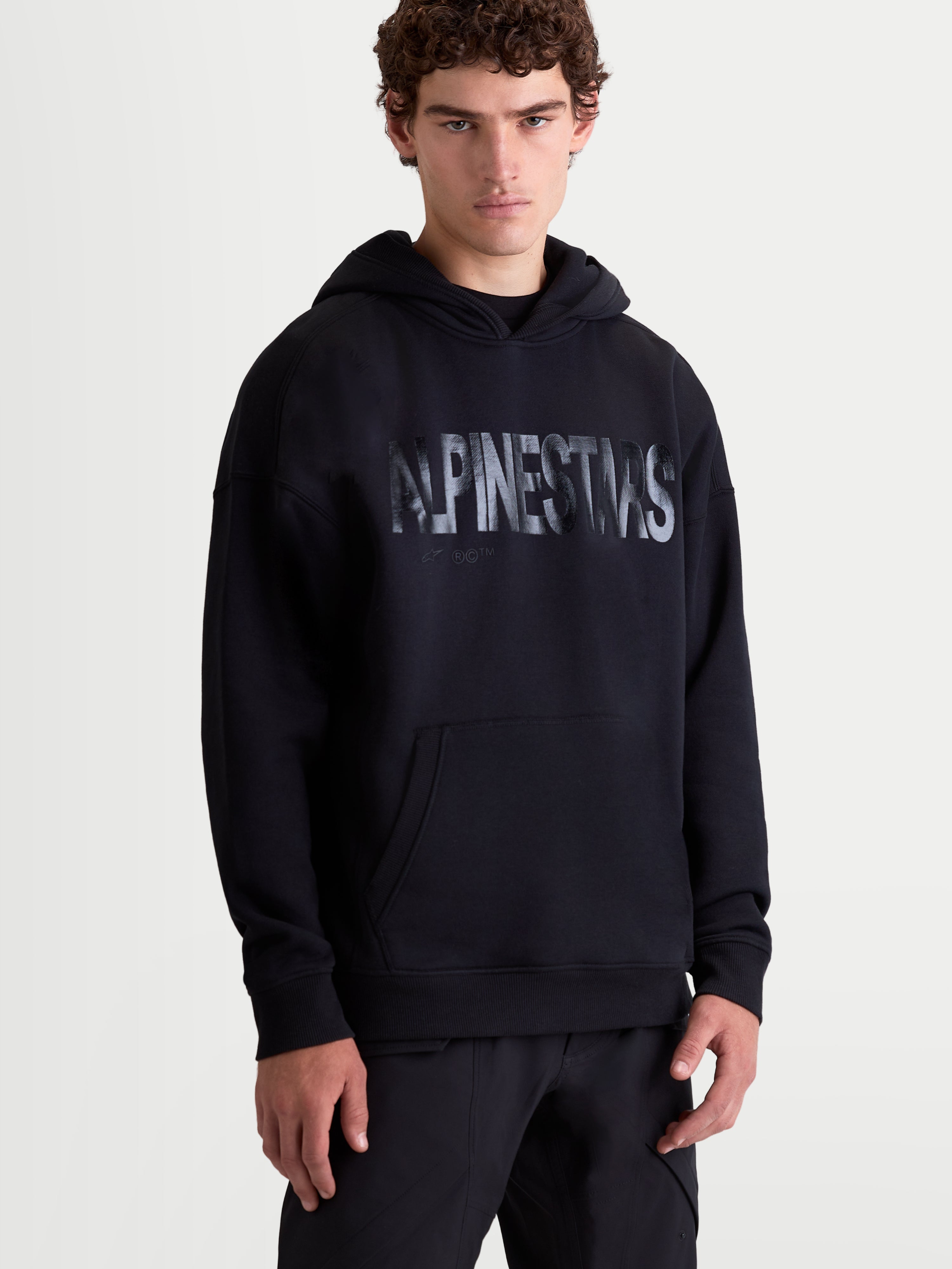 Alpinestars Sudadera Con Capucha Shaw Oversized, sudadera de estilo casual sportswear para hombre, negra, con logotipo texturizado en el pecho, bolsillo canguro y capucha forrada, mezcla de algodón y poliéster reciclado, vista frontal sobre modelo