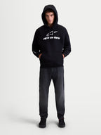 Alpinestars Prelude Oversized Hoodie, sudadera con capucha de estilo deportivo para hombre, color negro con logotipos blancos en el pecho y la manga, ajuste oversized con bolsillo canguro, confeccionada en forro polar de algodón y poliéster reciclado, mostrada en modelo.