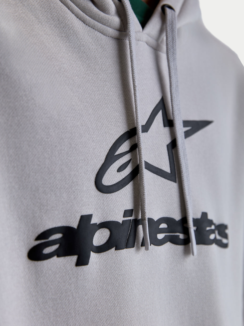 Alpinestars Prelude Oversized, sudadera con capucha, detalle en primer plano del logotipo frontal en relieve y gráfico de estrella en negro sobre forro polar gris cemento, cordones planos, ropa deportiva premium unisex