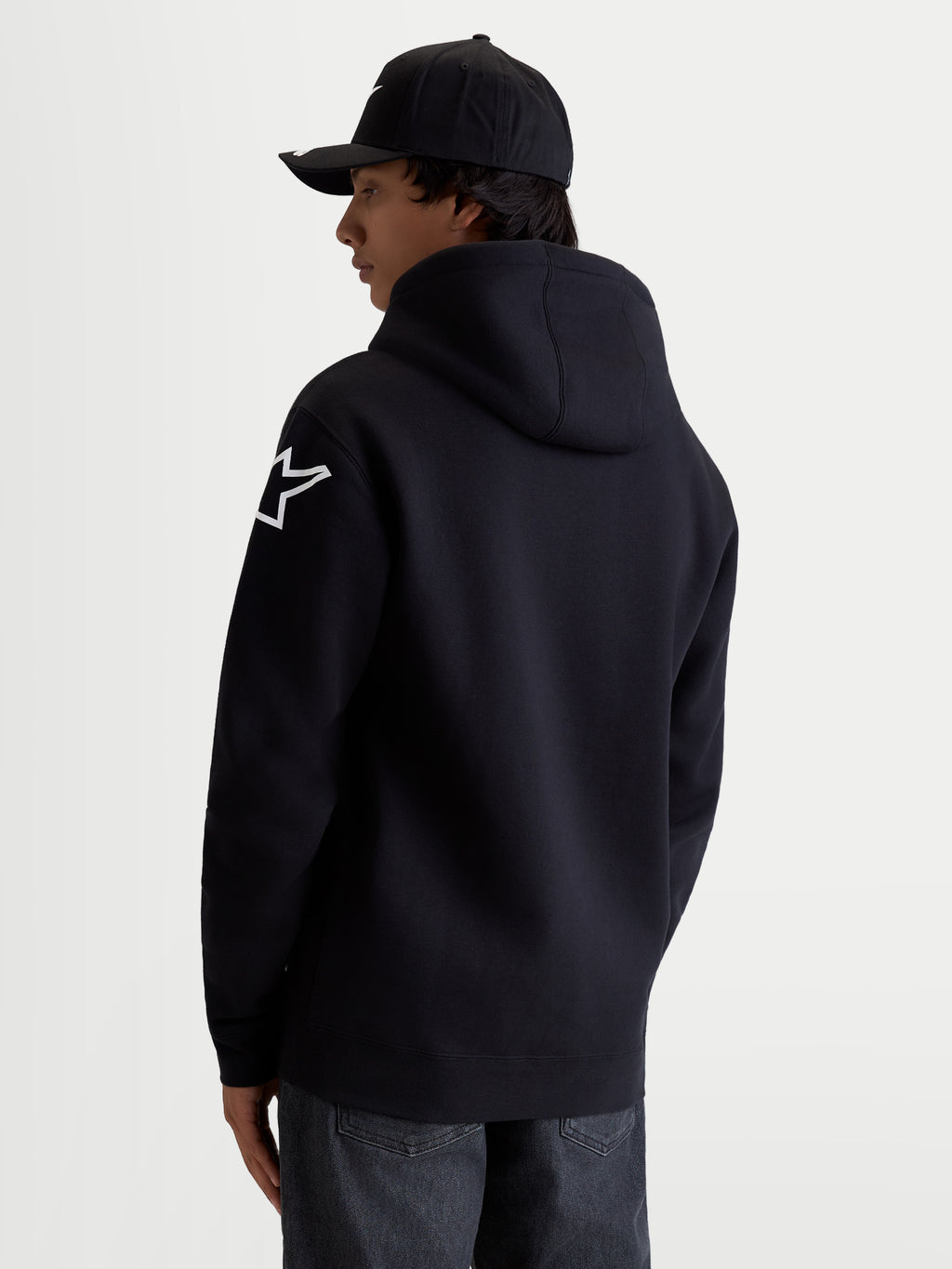 Alpinestars Sudadera con capucha Velocifier, sudadera de forro polar para hombre en color negro, con logotipo Astars blanco en el hombro, capucha forrada y puños de canalé, confeccionada en mezcla de algodón y poliéster reciclado, ropa deportiva de estilo casual para entusiastas del motorsport, vista trasera en modelo.