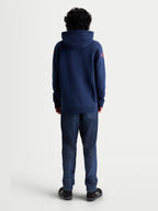 Alpinestars Velocifier, sudadera con capucha de forro polar, vista trasera en modelo, azul marino con logotipos rojos en los hombros, confeccionada en mezcla de algodón y poliéster reciclado, estilo casual inspirado en el motorsport