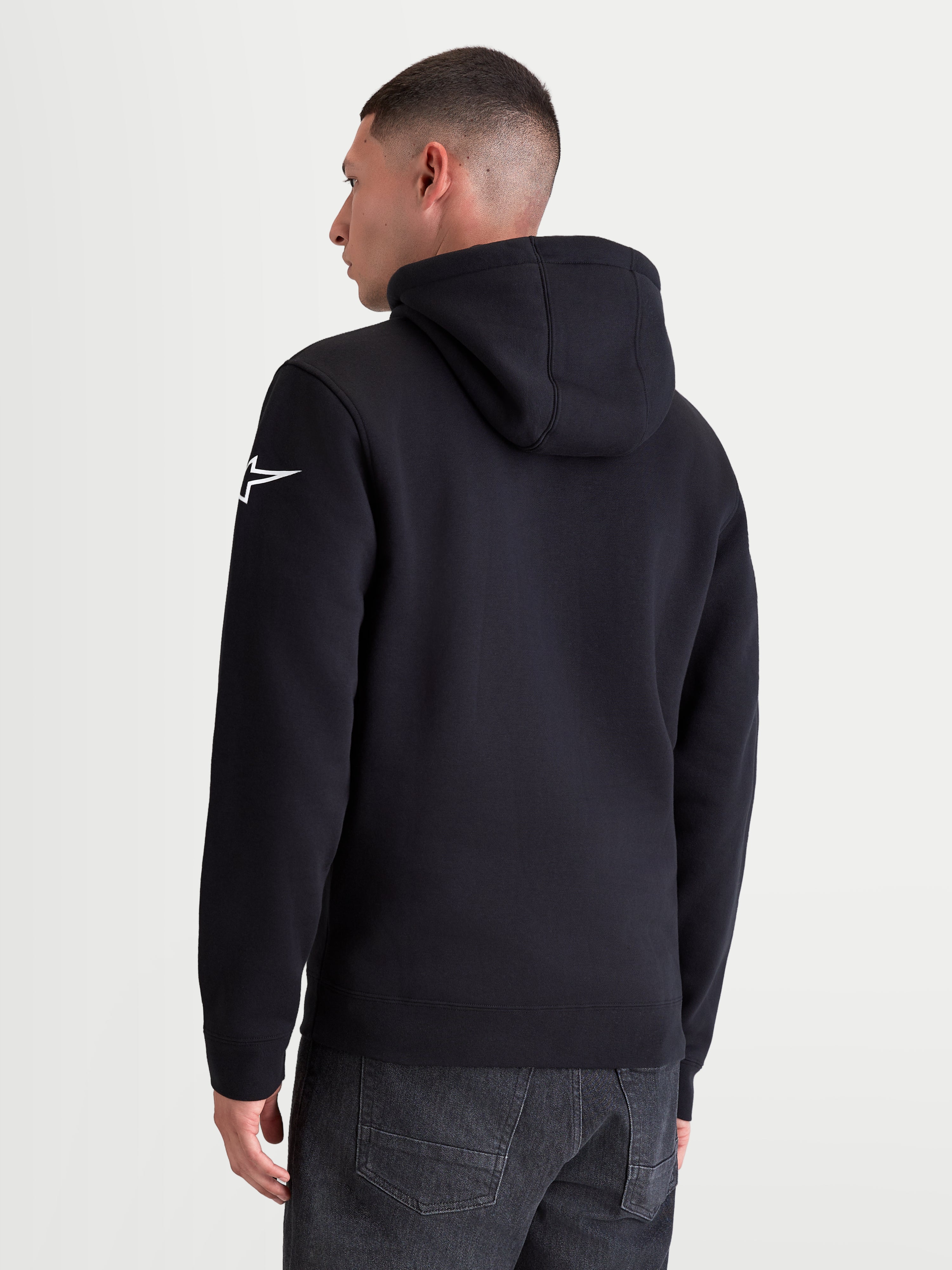 Alpinestars Race Wordmark, sudadera con capucha de forro polar, vista posterior en modelo, color negro con logotipo Ageless blanco en la manga izquierda, capucha y puños de canalé, mezcla de algodón y poliéster reciclado, ropa deportiva casual
