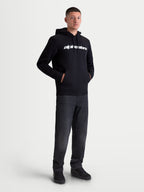 Alpinestars sudadera con capucha Race Wordmark, sudadera de forro polar para hombre, negra con logotipo lineal blanco en el pecho, capucha forrada con cordones y bolsillo tipo canguro, ropa deportiva casual de estilo motorsport, mostrada en modelo.