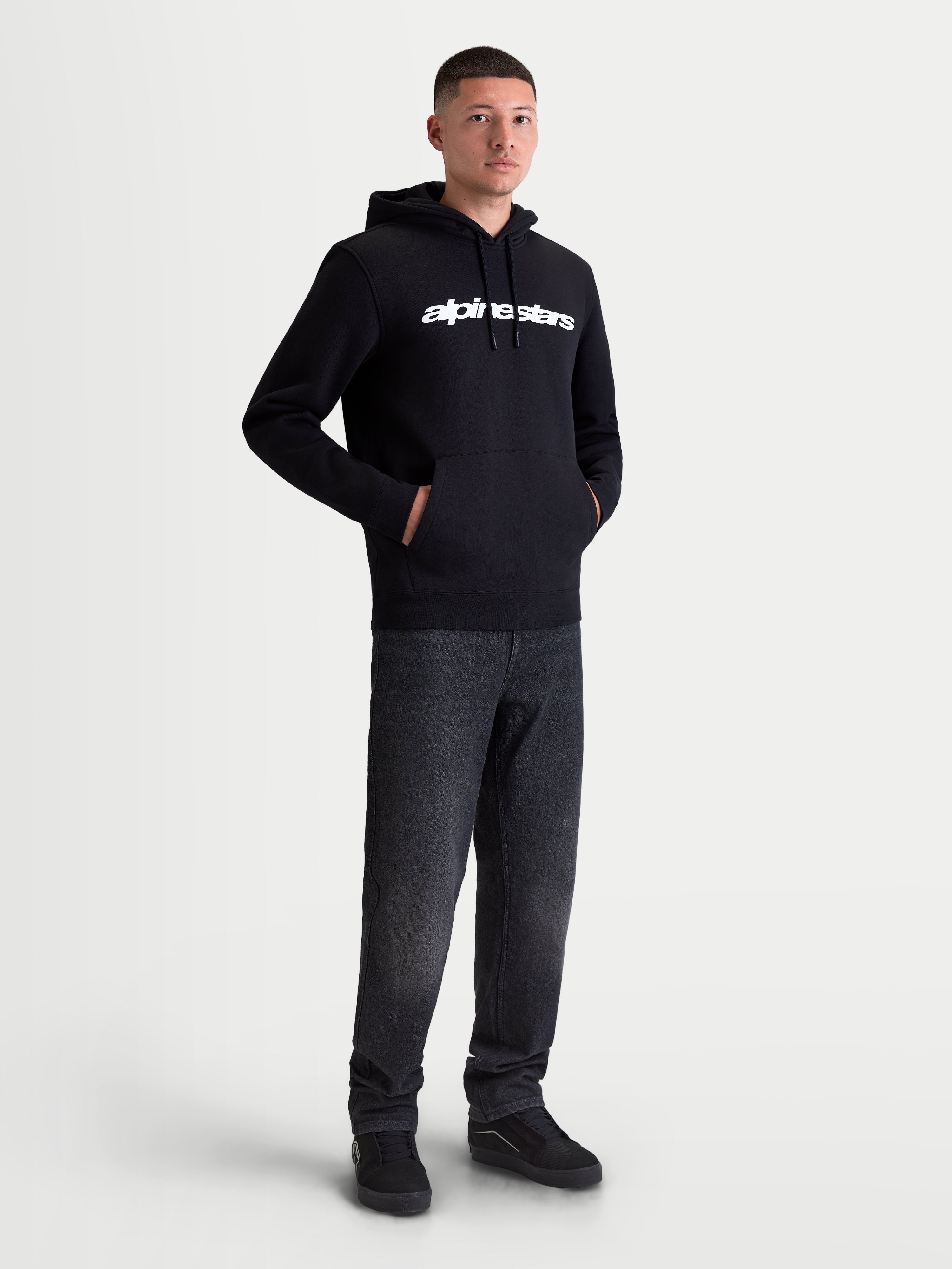 Alpinestars sudadera con capucha Race Wordmark, sudadera de forro polar para hombre, negra con logotipo lineal blanco en el pecho, capucha forrada con cordones y bolsillo tipo canguro, ropa deportiva casual de estilo motorsport, mostrada en modelo.