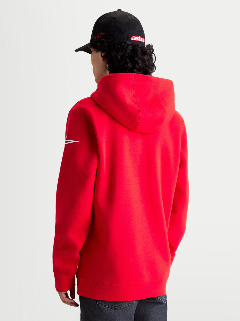 Alpinestars Sudadera con capucha Race Wordmark, forro polar tipo pulóver de ropa deportiva en rojo y blanco, vista trasera en modelo mostrando la capucha y el logotipo Ageless blanco en la manga, mezcla de algodón y poliéster reciclado para un estilo motorsport casual