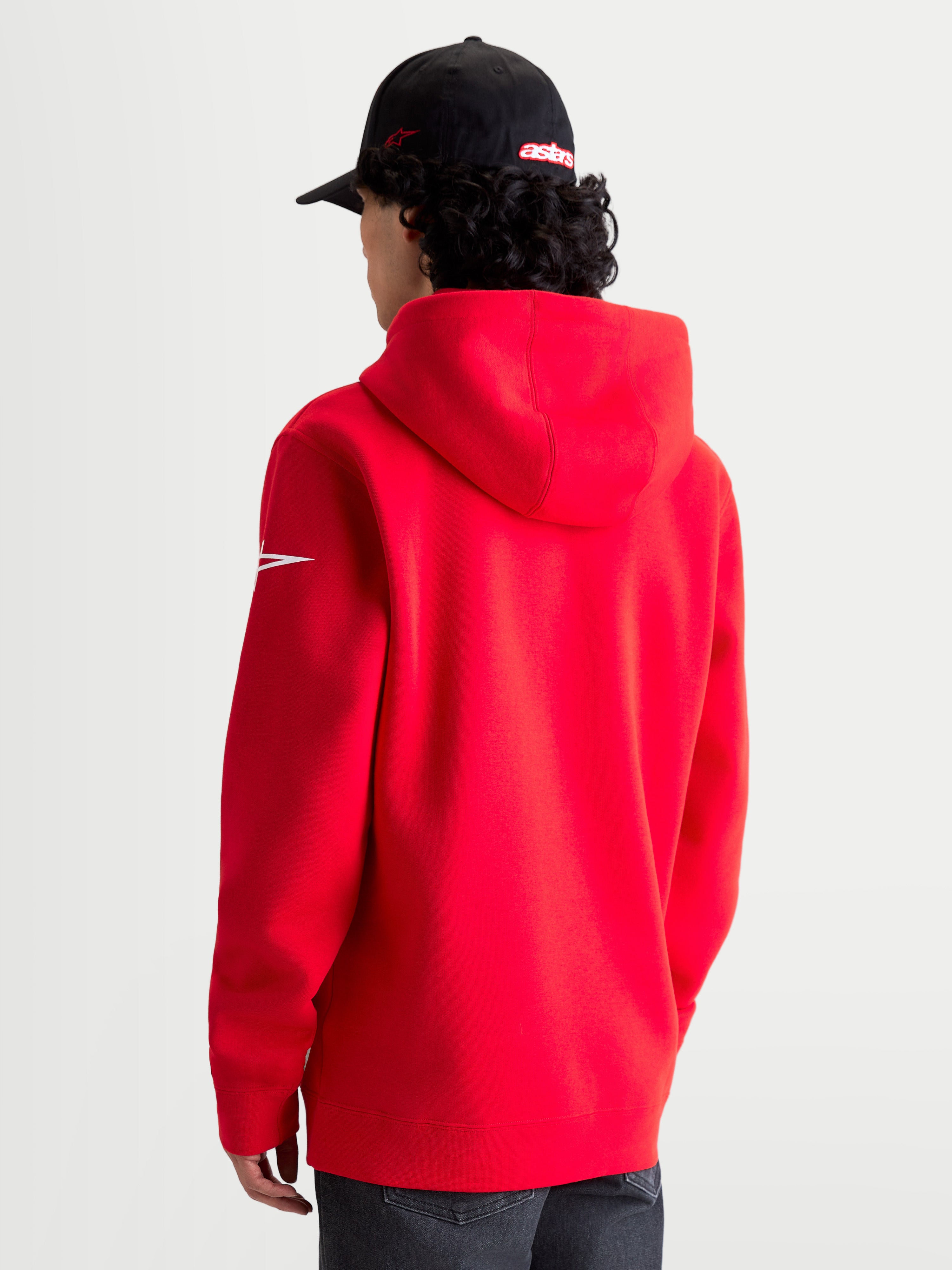 Alpinestars Sudadera con capucha Race Wordmark, forro polar tipo pulóver de ropa deportiva en rojo y blanco, vista trasera en modelo mostrando la capucha y el logotipo Ageless blanco en la manga, mezcla de algodón y poliéster reciclado para un estilo motorsport casual