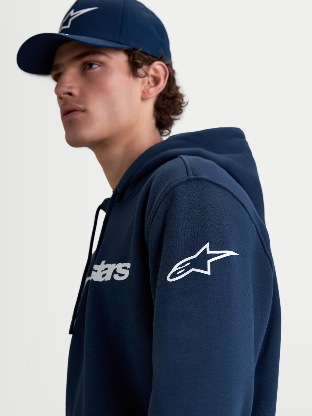 Alpinestars sudadera con capucha Race Wordmark, sudadera de forro polar para hombre, azul y blanca, con logotipo Ageless blanco en la manga y Race Wordmark en el pecho, confeccionada en algodón y poliéster reciclado, ropa deportiva de estilo casual, vista en modelo.