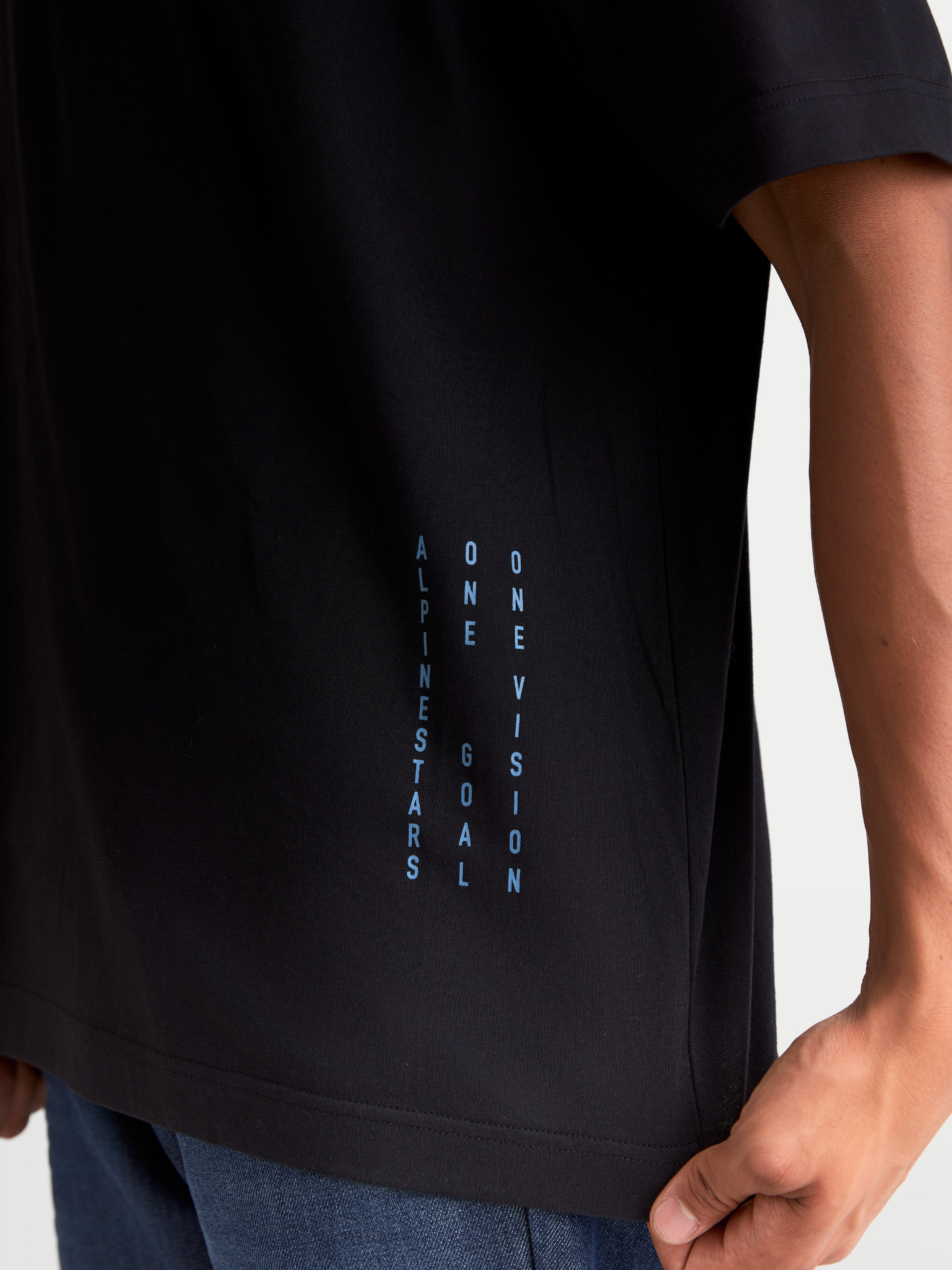 Alpinestars Chalk Oversized CSF Tee, Casual Motorsport Sportswear T-Shirt, Black with vertical Blue side branding text 'ALPINESTARS ONE GOAL ONE VISION', close-up detail shot on model.