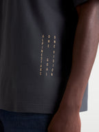 Alpinestars Camiseta Chalk Oversized CSF, camiseta de manga corta unisex, gris oscuro, detalle en primer plano del branding lateral vertical con el manifiesto 'ONE GOAL ONE VISION', tejido de mezcla de algodón y poliéster, ropa casual de inspiración motorsport.