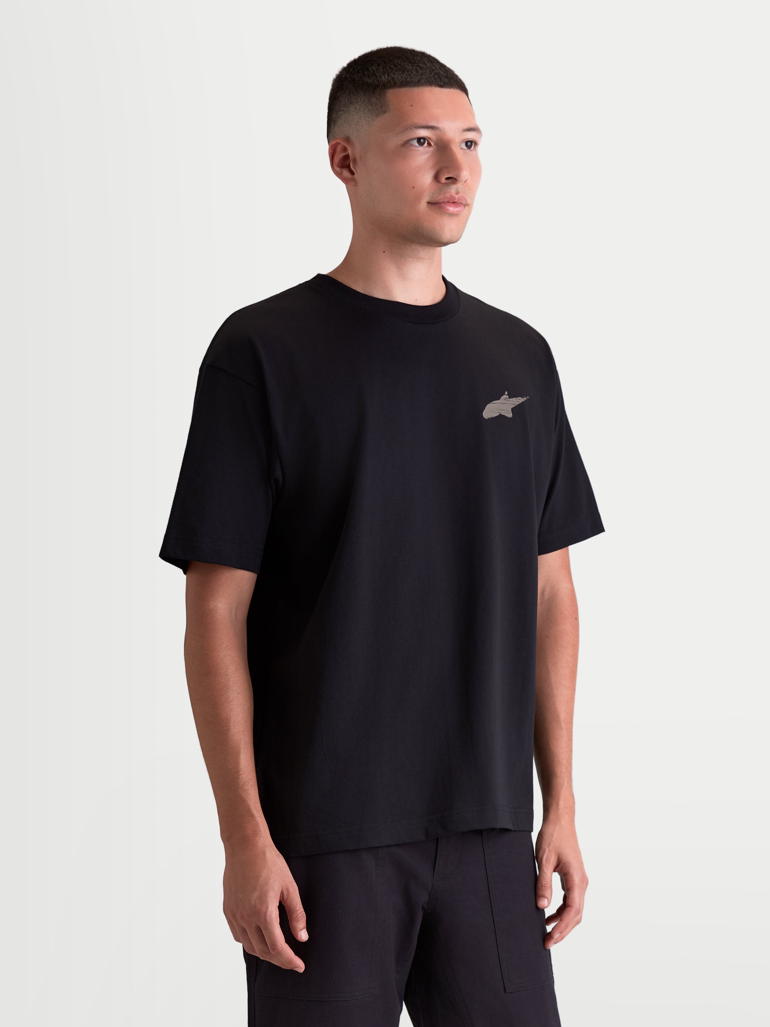 Alpinestars camiseta Checkback Oversized CSF, camiseta de mangas cortas para hombre, negra, vista en modelo con ajuste oversize relajado y pequeño logotipo Astars frontal, confeccionada en mezcla de algodón premium, ropa deportiva de estilo casual inspirado en el motorsport