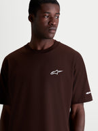 Alpinestars Mandate Oversized CSF, camiseta de mangas cortas de estilo casual y deportivo, marrón con logotipo Astars blanco en el pecho, ajuste relajado y holgado, confeccionada en mezcla de algodón y poliéster, detalle en modelo.