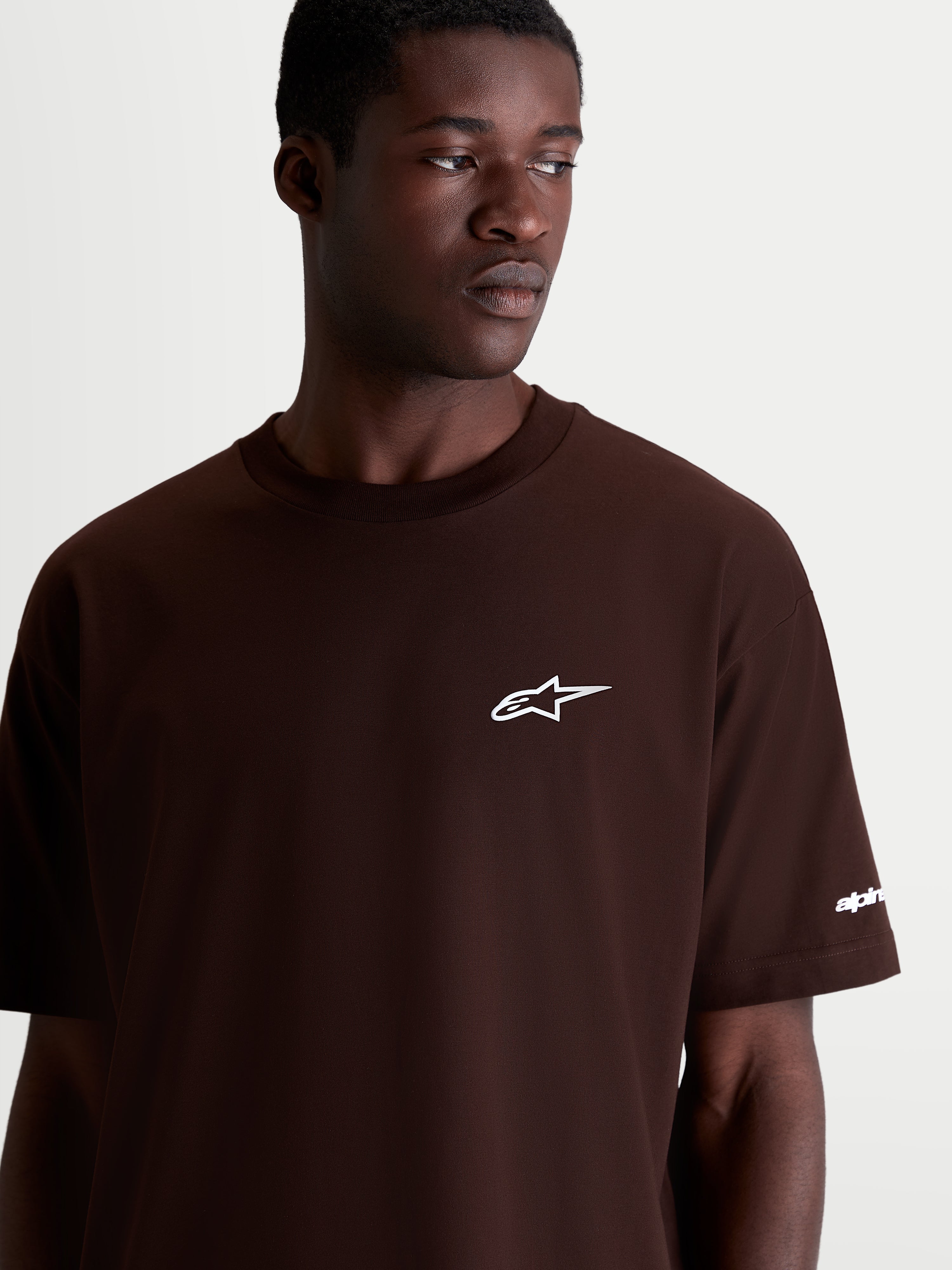 Alpinestars Mandate Oversized CSF, camiseta de mangas cortas de estilo casual y deportivo, marrón con logotipo Astars blanco en el pecho, ajuste relajado y holgado, confeccionada en mezcla de algodón y poliéster, detalle en modelo.
