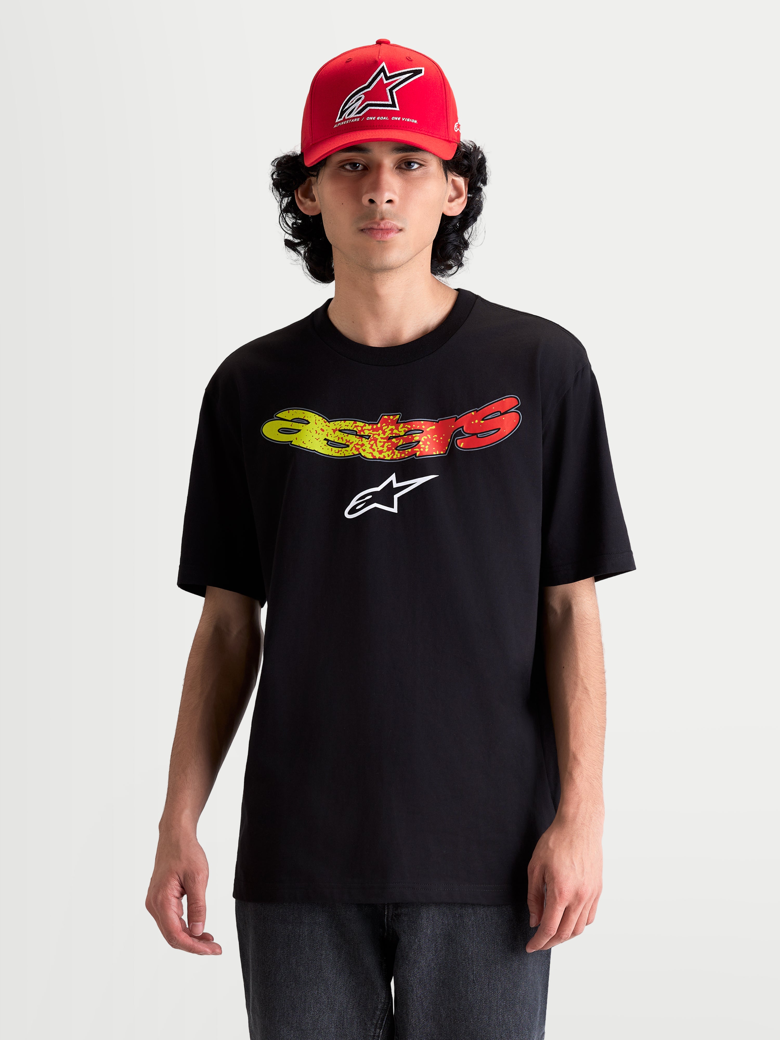 Alpinestars Elliptogrit CSF, camiseta de mangas cortas para hombre en modelo, negra con gráfico frontal de la palabra Astars en degradado rojo y amarillo, ropa deportiva casual de tacto suave