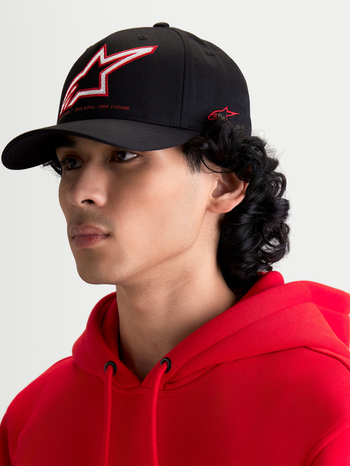 Alpinestars Gorra Lineout, gorra de béisbol negra con visera curva, corona estructurada con logotipo Astars bordado en rojo y blanco, mostrada en un modelo, ropa deportiva