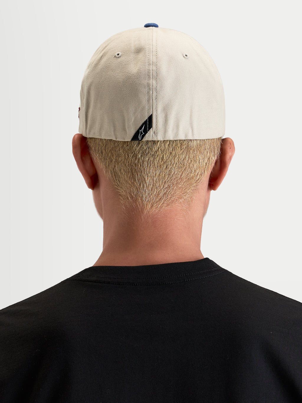 Gorra County Canvas Alpinestars, gorra sportswear casual, color arena y azul, vista trasera en modelo mostrando el ajuste flex-back y el detalle sutil de la etiqueta trasera