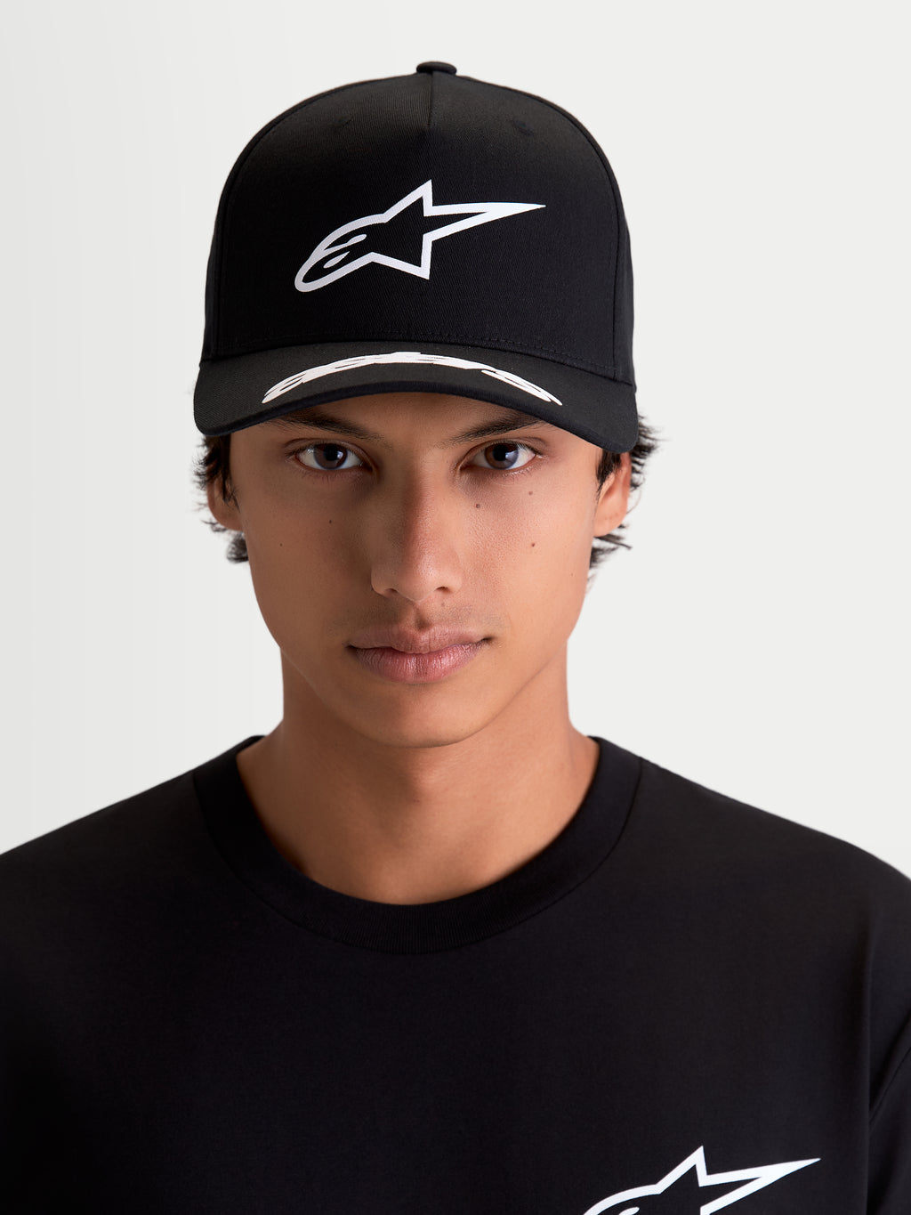 Alpinestars Arclight, gorra de estilo motorsport y sportswear, negra y blanca, vista frontal en modelo, con logotipo Astars en relieve blanco sobre corona estructurada, visera curva con detalles y tejido de sarga premium.