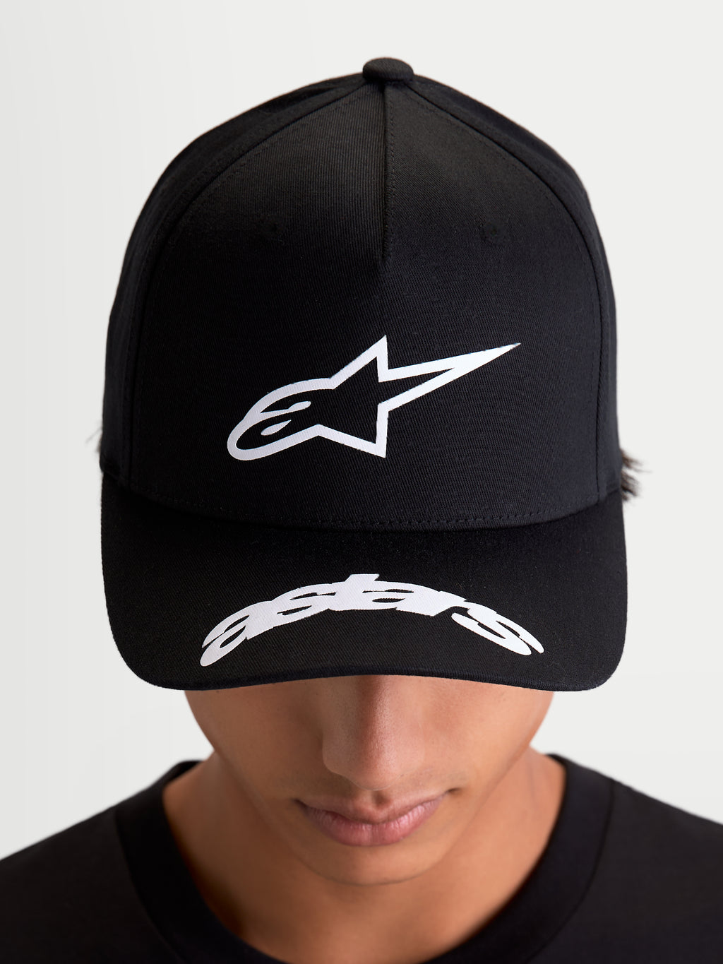 Alpinestars Gorra Arclight, gorra de béisbol de sportswear negra, vista frontal en modelo con logotipo Astars blanco en relieve sobre corona estructurada y logotipo curvado en la visera, estilo casual de motorsport