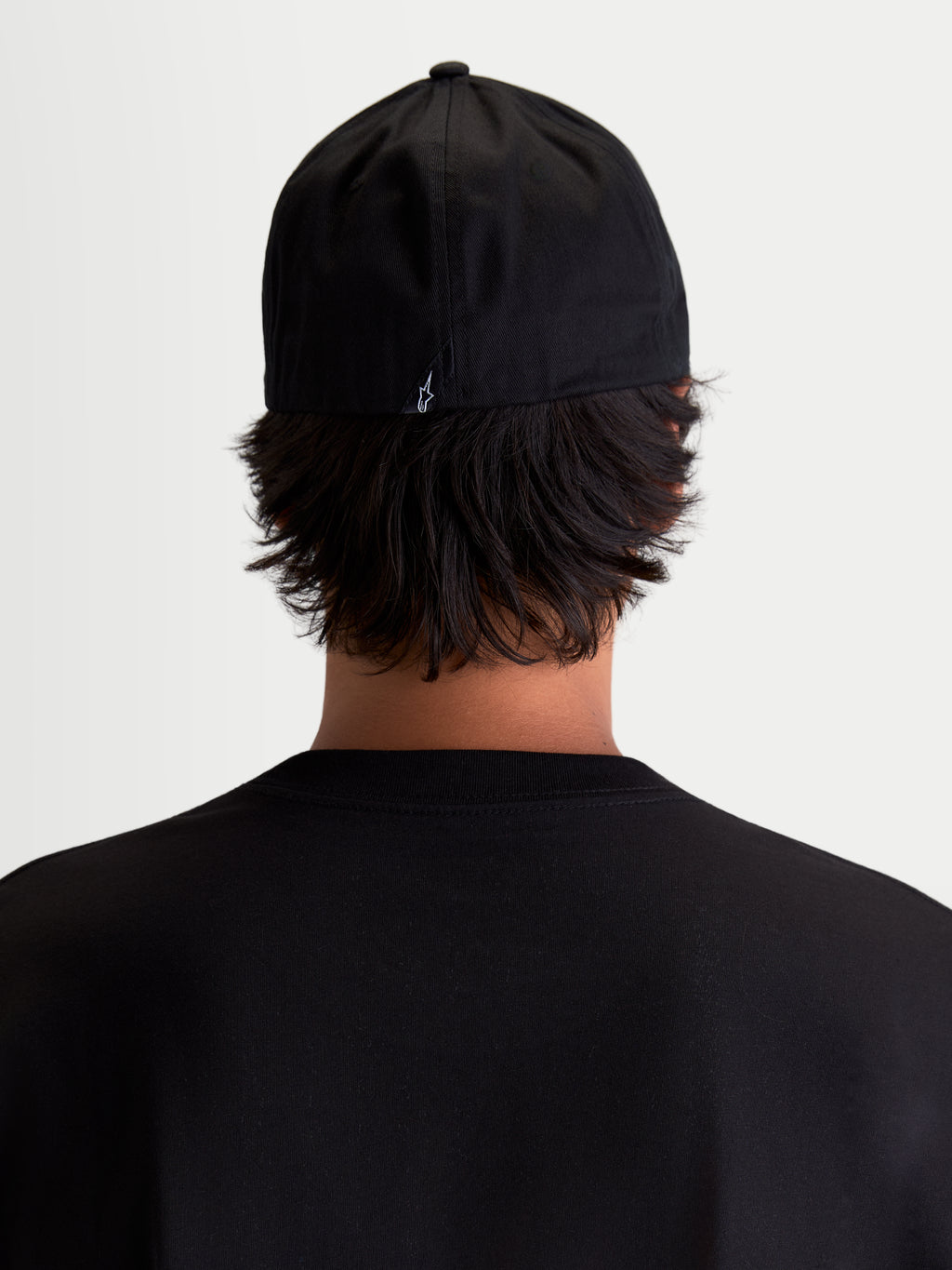Alpinestars Gorra Arclight, gorra de estilo deportivo negra, vista trasera sobre modelo, con pequeño logotipo Astars blanco en la parte posterior, confeccionada en sarga de algodón resistente para uso diario y casual