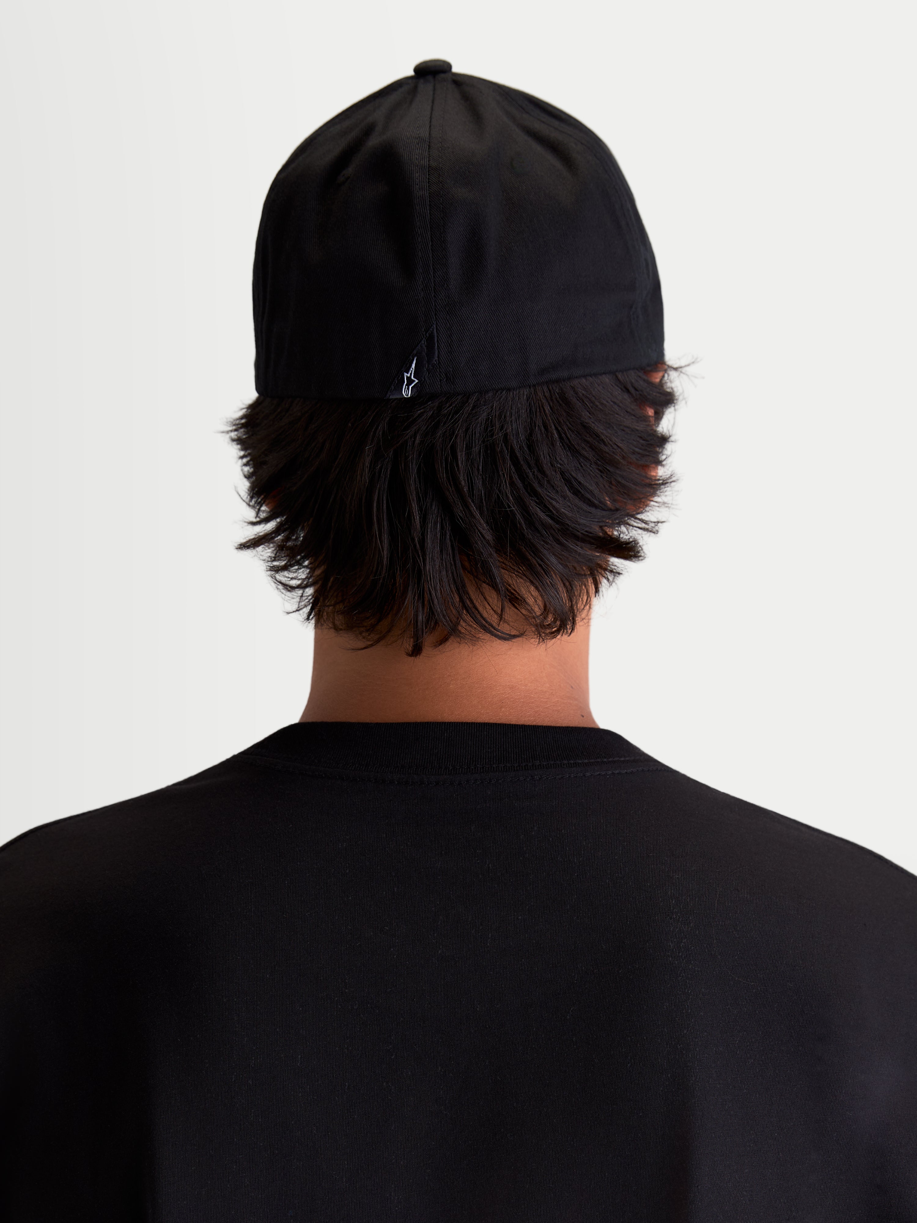 Alpinestars Gorra Arclight, gorra de estilo deportivo negra, vista trasera sobre modelo, con pequeño logotipo Astars blanco en la parte posterior, confeccionada en sarga de algodón resistente para uso diario y casual