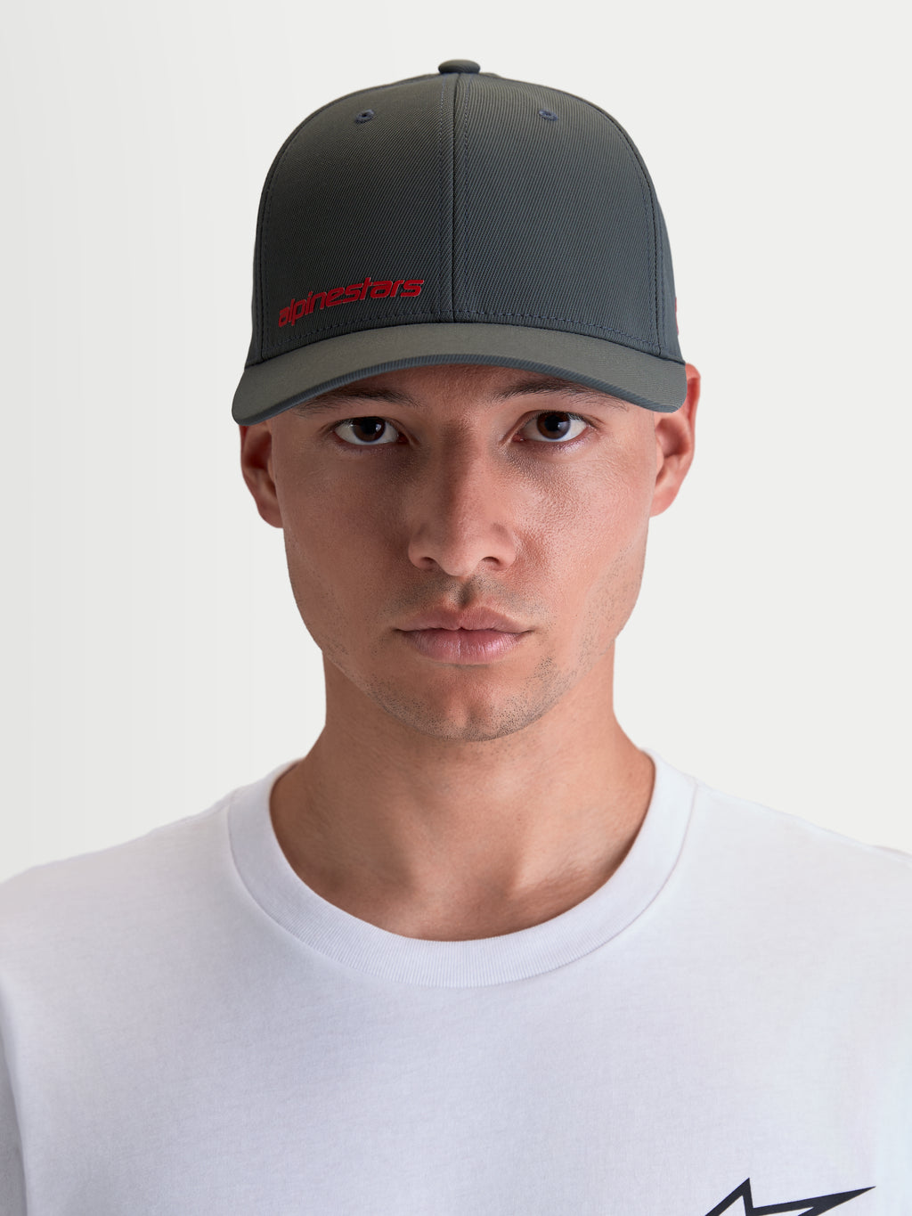 Alpinestars Gorro Points, gorra sportswear con visera curva para hombre y mujer, vista frontal en modelo, gris oscuro con logotipo Alpinestars rojo, tejido ligero de nylon tactel con ajuste flex-back