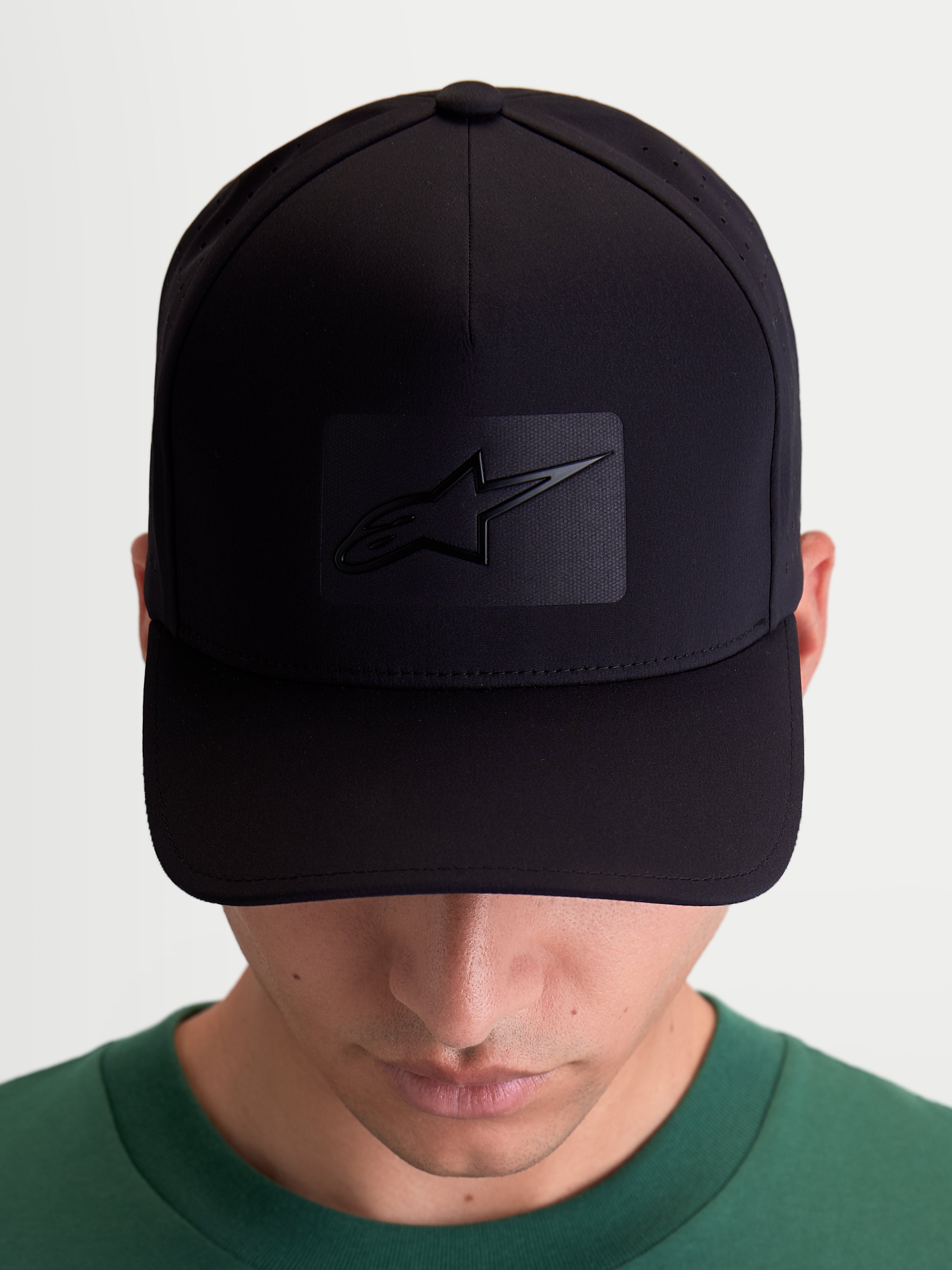 Gorra Alpinestars Algo Perf Ajustable, gorra deportiva de estilo motorsport, negra, fabricada en tejido técnico con perforaciones laterales, visera curva y corona estructurada, vista frontal en modelo con el logotipo Astars con soldadura sónica.