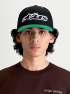 Alpinestars Retro Snapback, gorra de estilo sportswear y lifestyle, negra y verde, con visera curva, corona estructurada y logotipo Astars bordado con pespunte verde, vista frontal en modelo